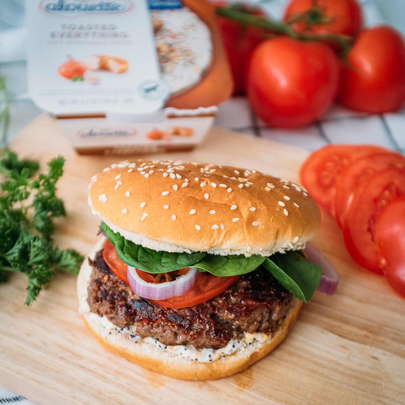 Hamburger with Aouette toasted everything, a patty, tomato, onion, salad